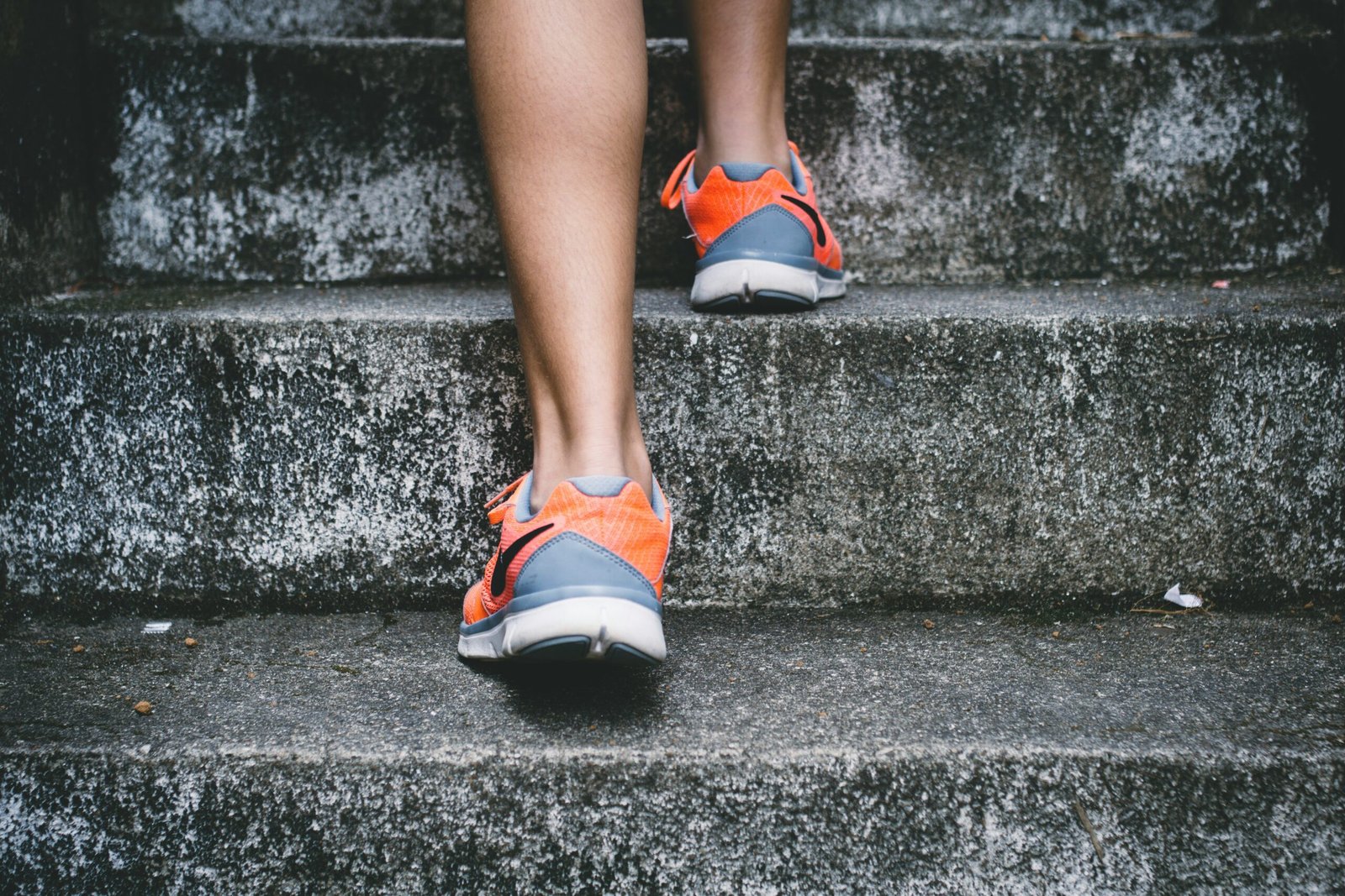 person wearing orange and person wearing orange and gray Nike shoes walking on gray concrete stairs